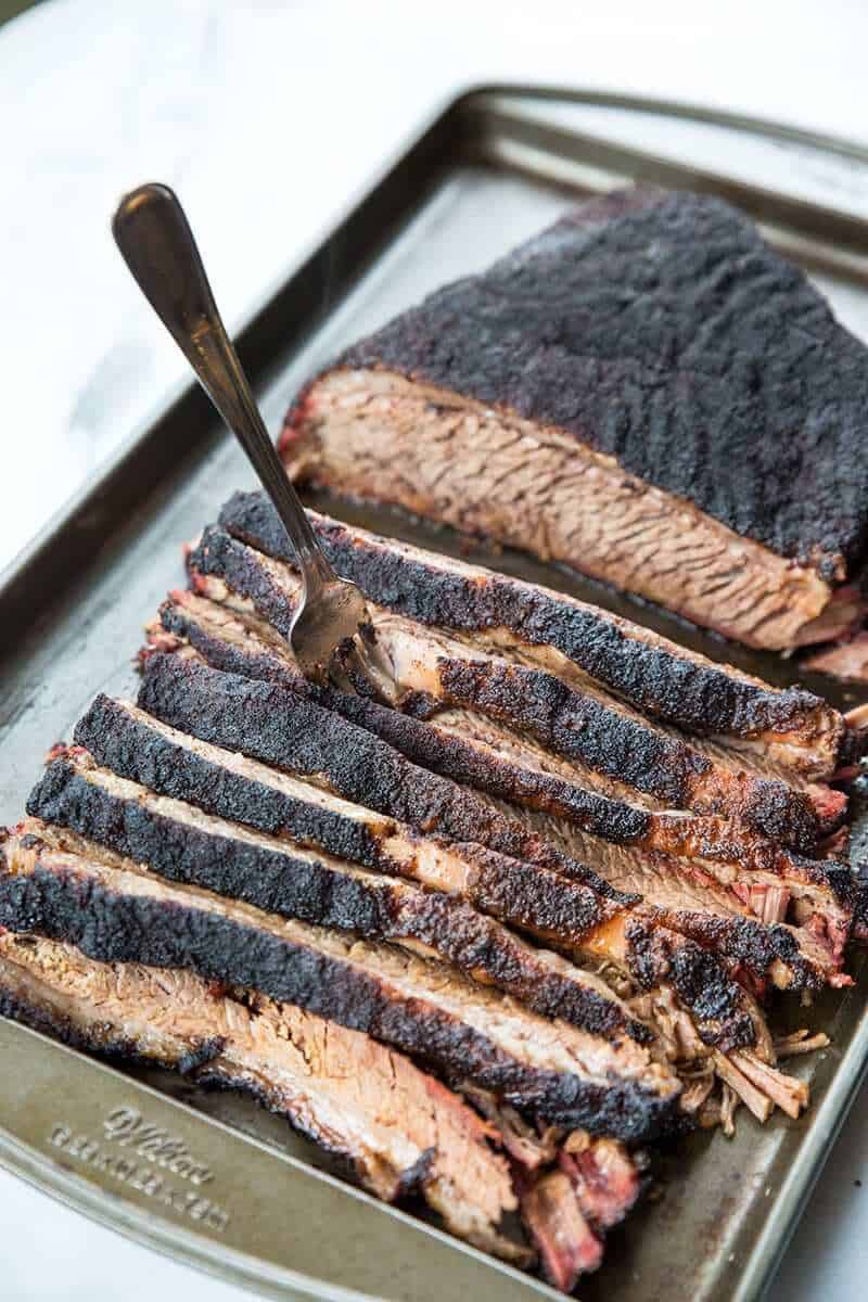Sliced Dry Rub Smoked Brisket in a pan with fork in one of the slices