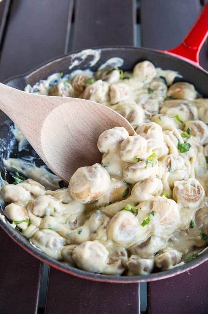  A wooden spoon in Creamy Parmesan Garlic Sauteed Mushrooms in a red skillet