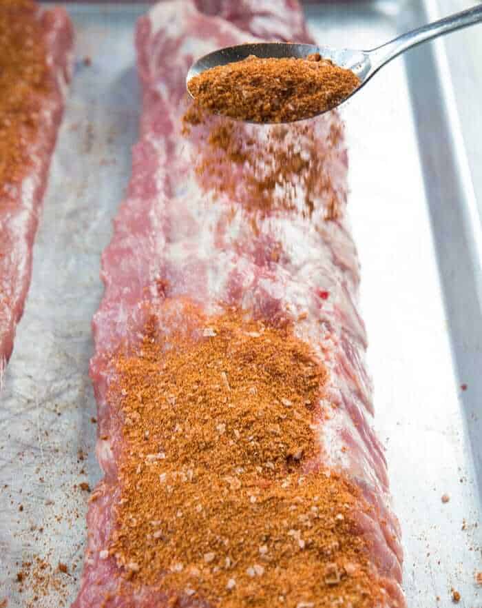 Sprinkling dry rib rub on top of raw pork ribs