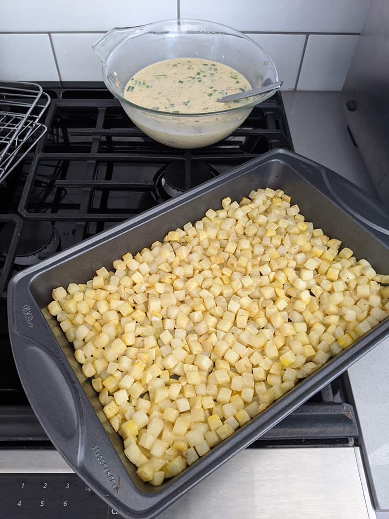 hash brown crust in an aluminum baking pan on a stove top with egg mixture in a bowl above it.