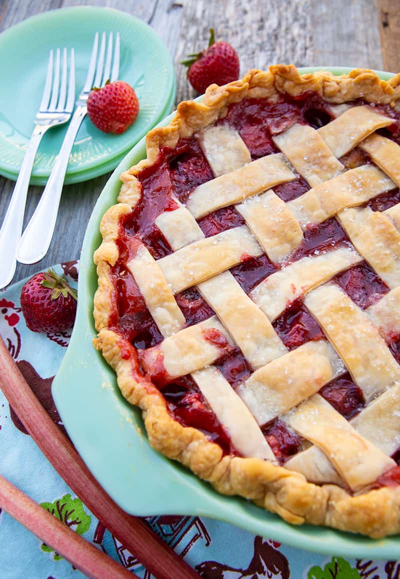 Strawberry Rhubarb Pie in a baking dish, serving plates with fork and fresh strawberry on the side