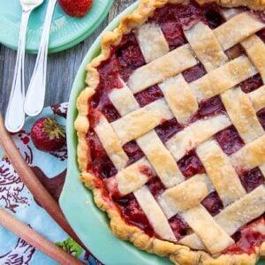 Strawberry Rhubarb Pie in a baking dish, serving plates with fork and fresh strawberry on the side