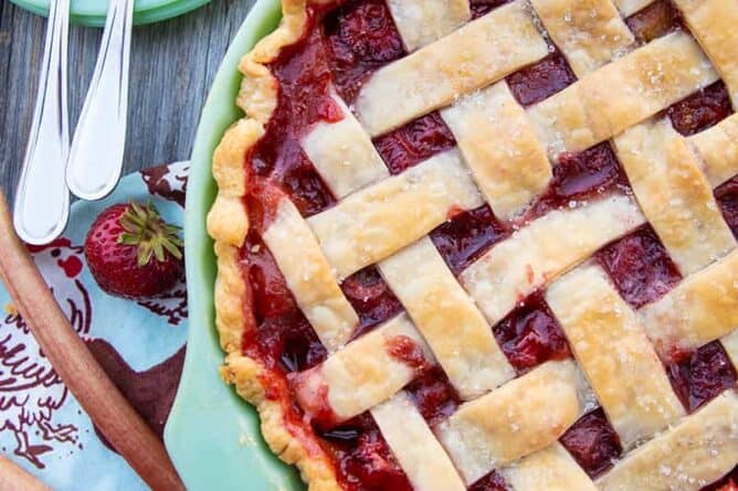 Strawberry Rhubarb Pie in a baking dish, serving plates with fork and fresh strawberry on the side