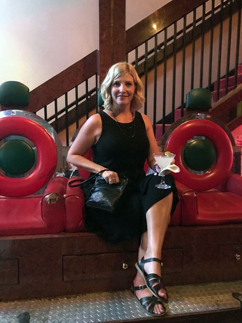Lady in black (Nicole) holding a glass of gimlet and sitting in shoeshine chairs