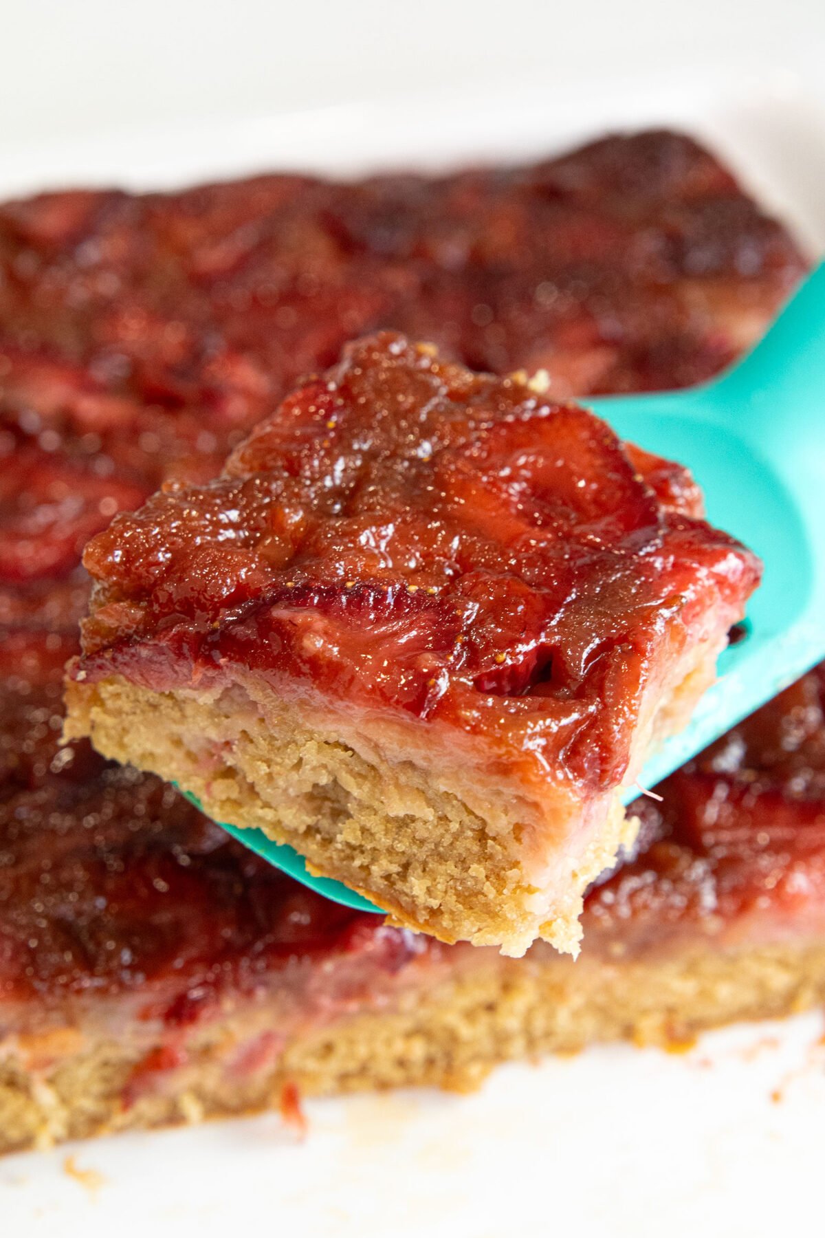 close up of a slice of Strawberry rhubarb upside down cake on a teal lifter