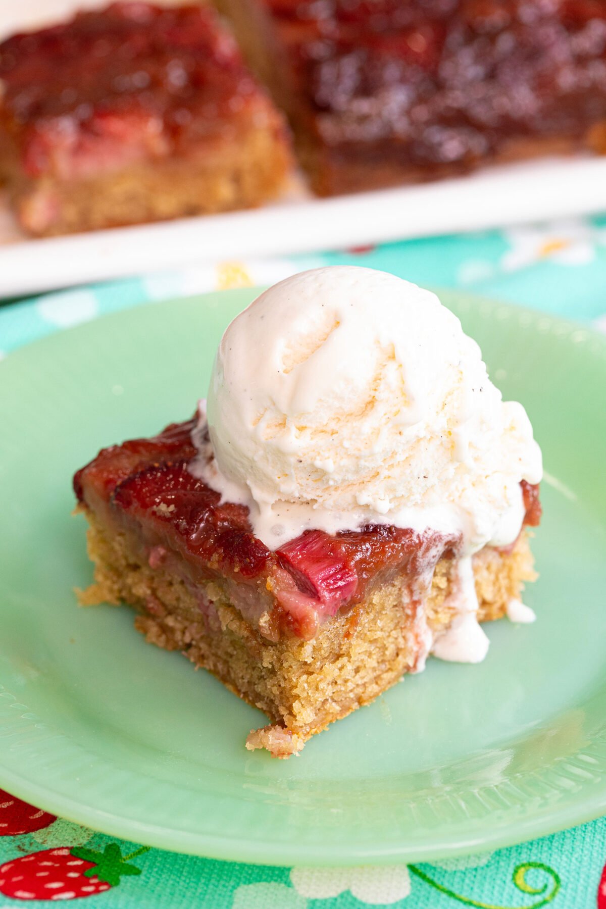 a slice of Strawberry rhubarb upside down cake on a green plate topped off with a  large scoop of vanilla ice cream on top. 