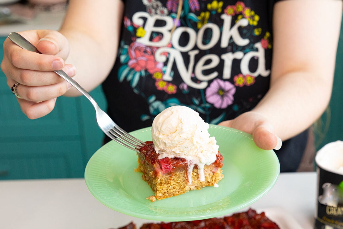 Strawberry rhubarb upside down cake on a green plate with a big scoop of vanilla ice cream on top