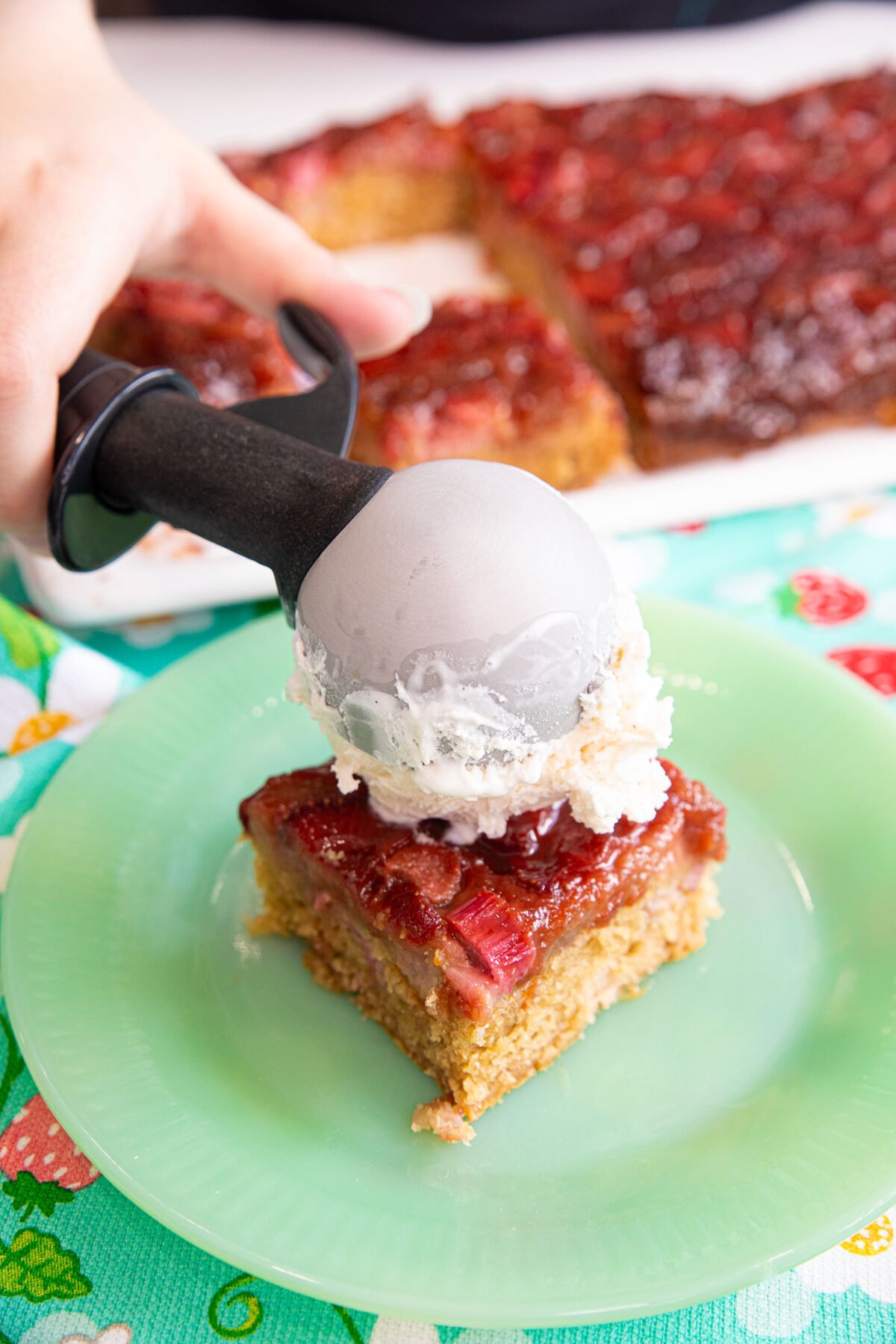 close up of a big scoop of vanilla ice cream being put on a slice of Strawberry rhubarb upside down cake