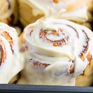 close up of a cinnamon bun in a pan with cream cheese icing slathered on top