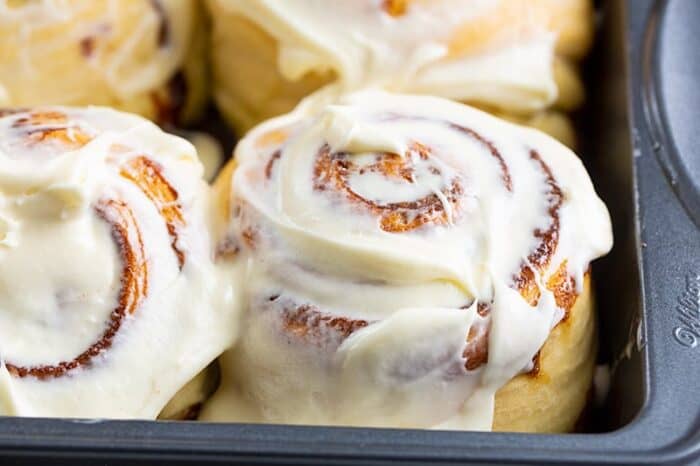 close up of a cinnamon bun in a pan with cream cheese icing slathered on top