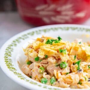 tuna casserole in a large white plate, with green peas and potato chips topping Red Harvest Pyrex casserole at the back