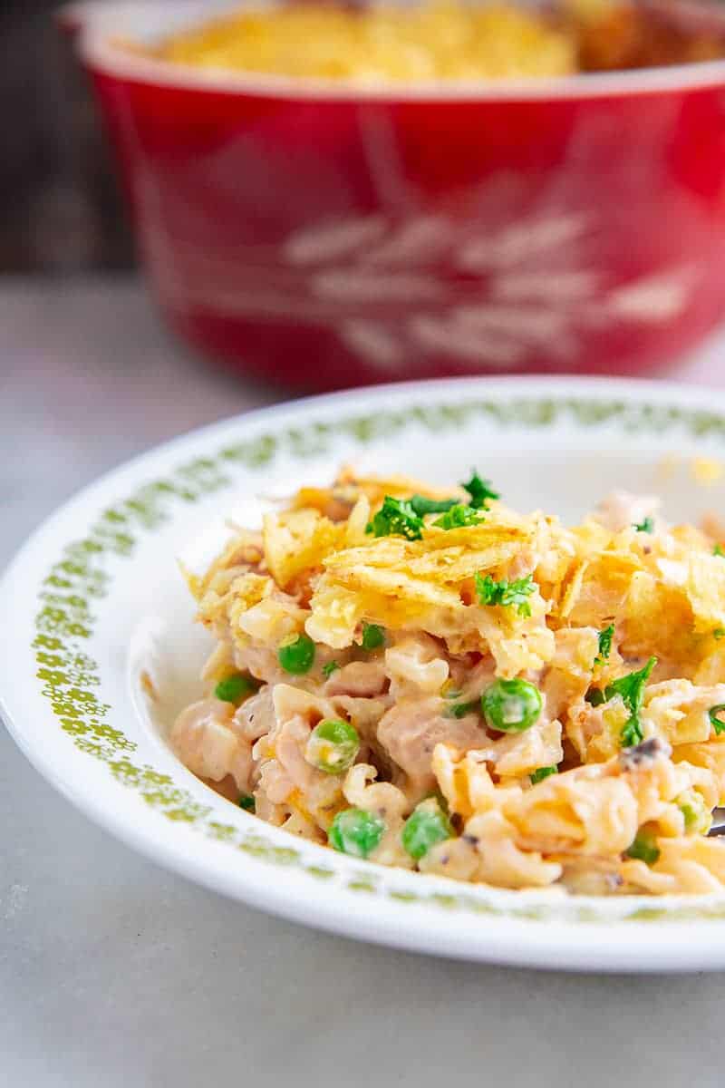 close up tuna casserole in a large white plate, with green peas and potato chips topping Red Harvest Pyrex casserole at the back