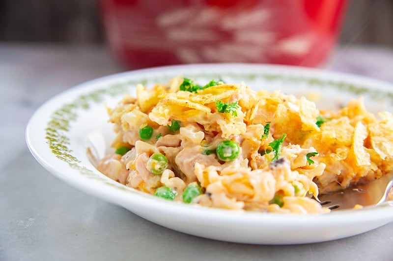 tuna casserole in a large white plate, with green peas and potato chips topping Red Harvest Pyrex casserole at the back