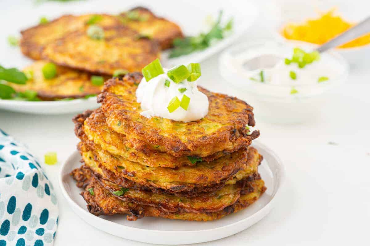 zucchini fritters on a white plate with sour cream on top of them