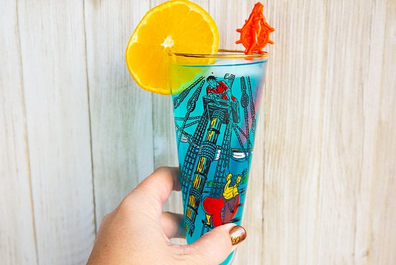 A blue AMF cocktail drink garnished with an orange slice that's in a vintage pirates motif glass