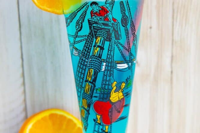 A blue AMF cocktail drink garnished with an orange slice that's in a vintage pirates motif glass