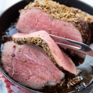 a meat fork with a slice of Herb & Garlic Bottom Round Roast in a red skillet