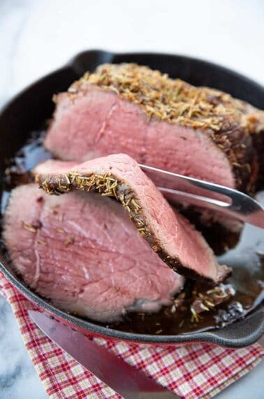 a meat fork with a slice of Herb & Garlic Bottom Round Roast in a red skillet