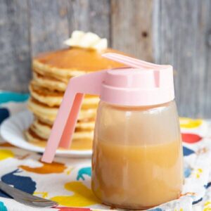 close up of Brown Sugar Sauce in a small pitcher like container, stack of pancakes in white plate on the background