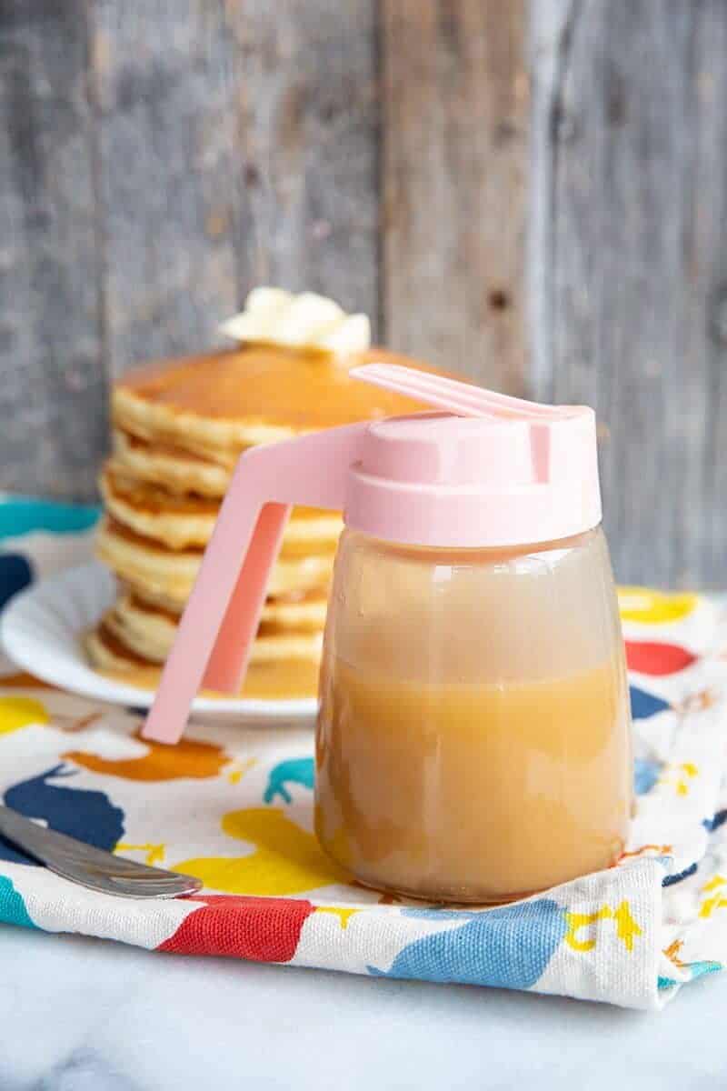 close up of Brown Sugar Sauce in a small pitcher like container, stack of pancakes in white plate on the background