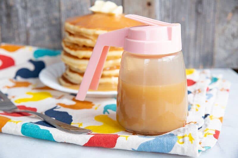 Brown Sugar Sauce for pancakes in a small pitcher like container, stack of pancakes in white plate on the background