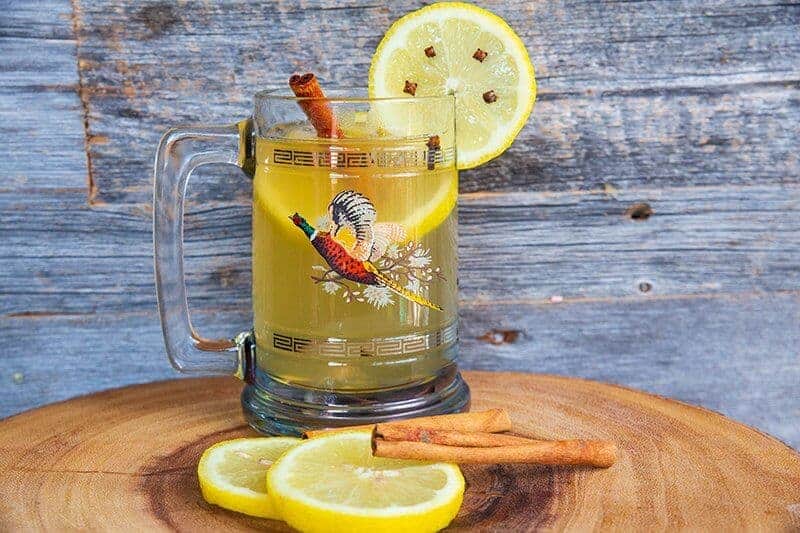 A classic hot toddy made with Scottish whisky in a vintage pheasant glass mug garnish with cinnamon sticks and slices of lemon