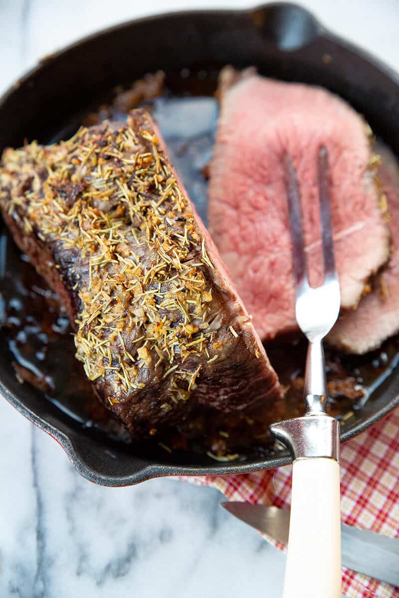 close up slice of Herb & Garlic Bottom Round Roast in a red skillet 