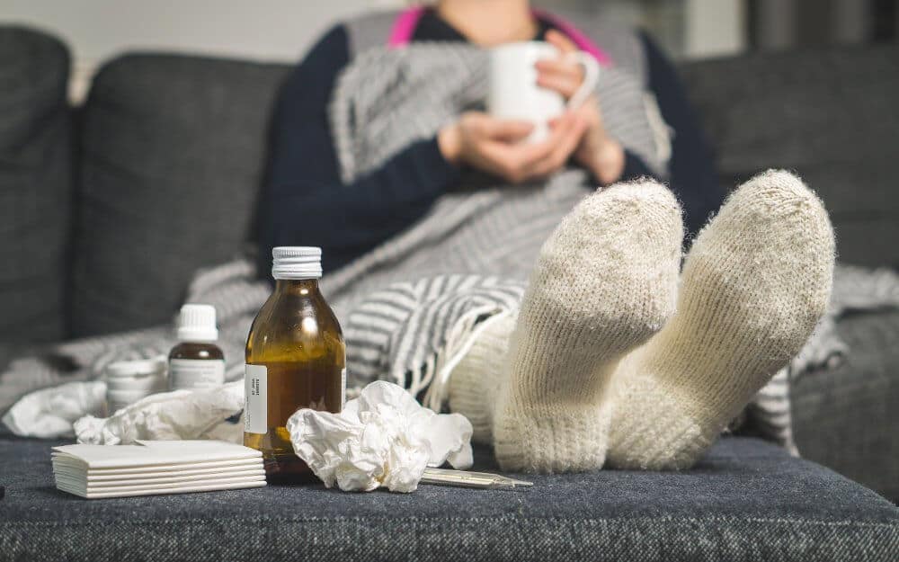 person with sign of colds, bottle of medicines and tissue on sofa bed