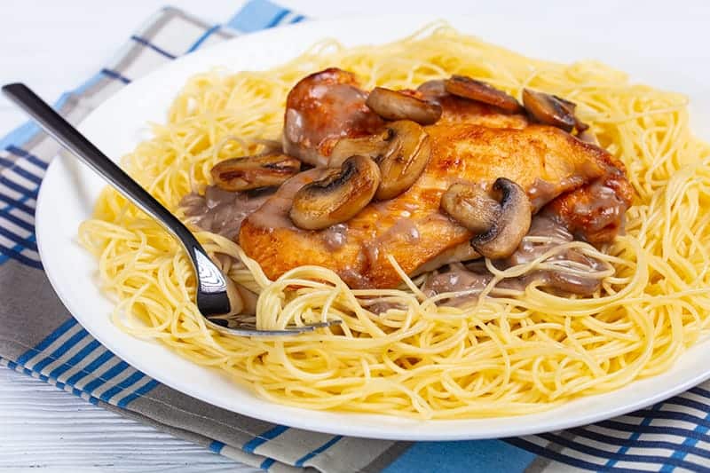 checkered blue kitchen towel underneath white plate with Chicken Marsala on angel hair pasta and a fork on it