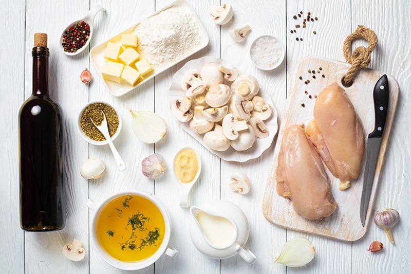 Chicken Marsala ingredients on a white wood background