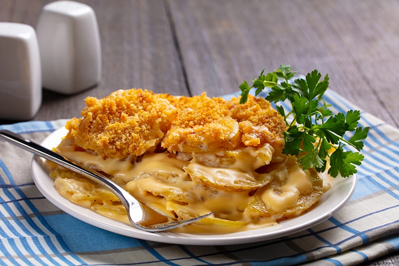 checkered blue tablecloth underneath a white plate with Potatoes Au Gratin topped with breadcrumbs