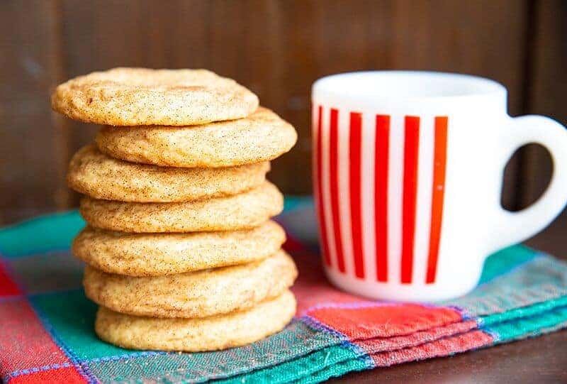 a stack of Classic Snickerdoodle and a stripe red mug with milk beside it placed under blue and pink colored kitchen cloth