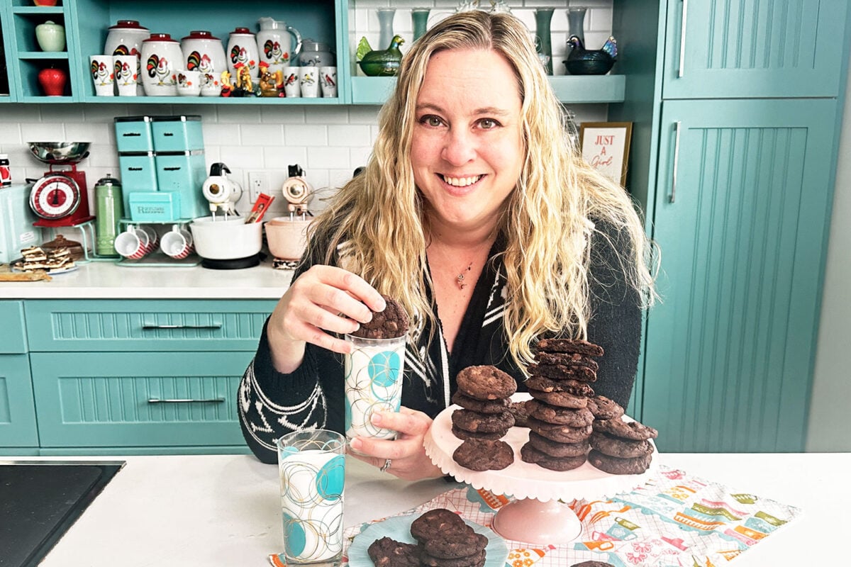 Dark Chocolate Cookies on a blue plate with Karlynn holding one and dipping a cookie in a glass of milk. 