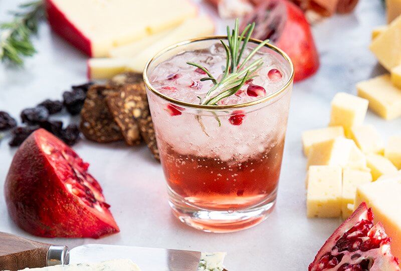 a glass of Pomegranate Gin Fizz in Cheeseboard with a sliced Pomegranate