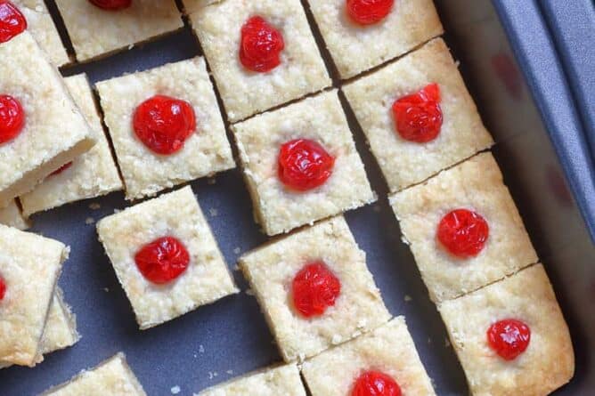 close up Shortbread Bites with candied cherries on top in a large baking sheet