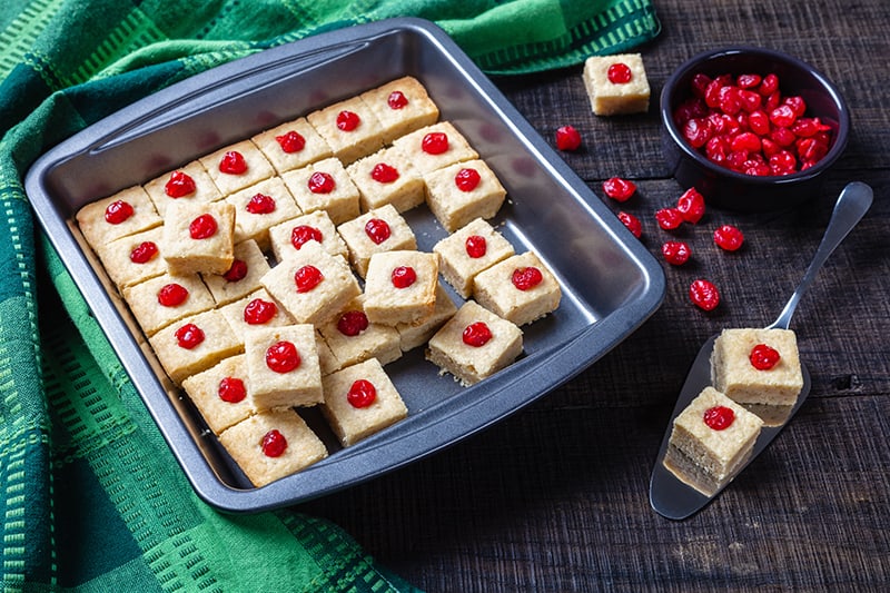 large baking sheet with Shortbread Bites with candied cherries, green tablecloth and some candied cherries at the side
