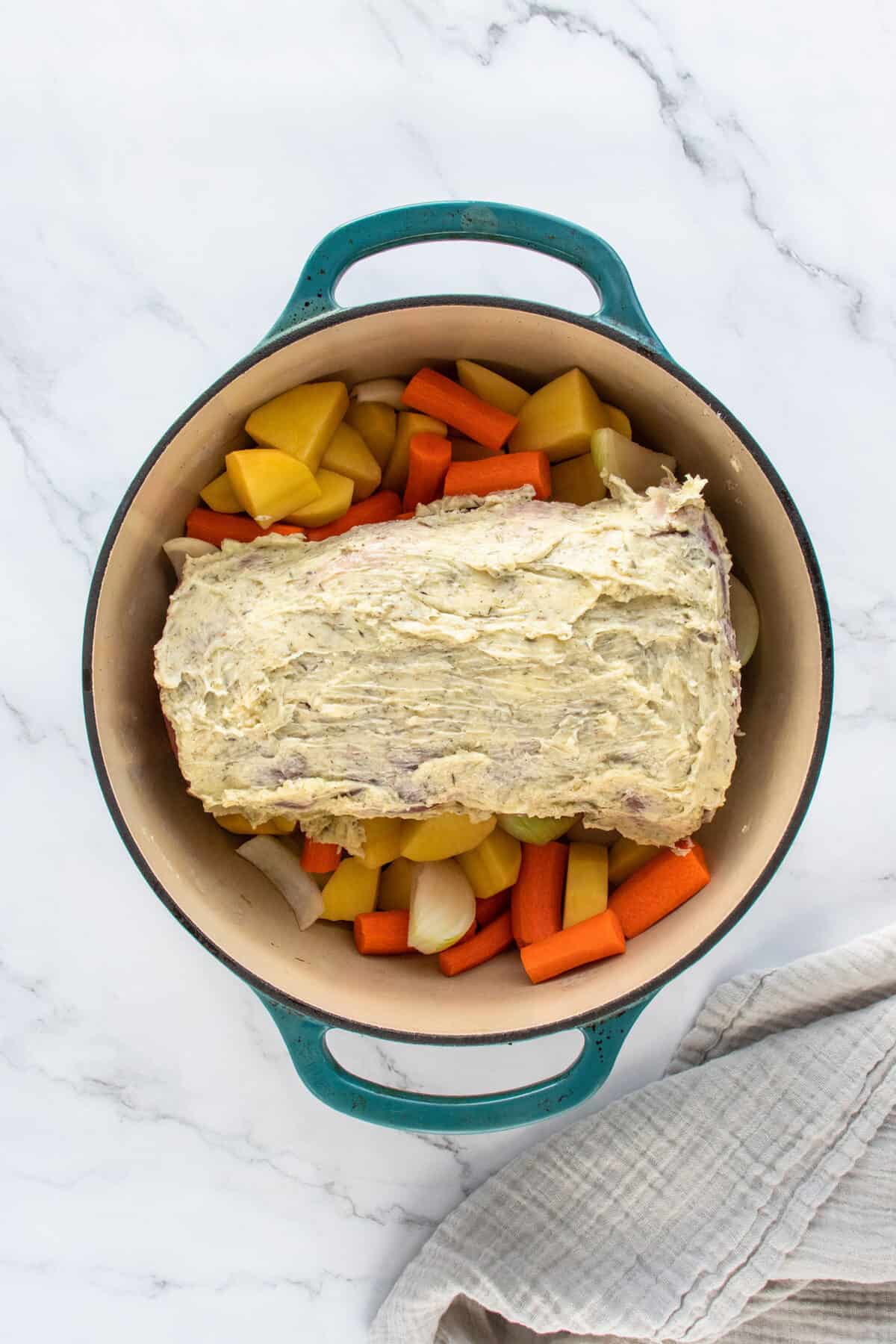buttered and herbed sirloin roast on top of vegetables in a Dutch oven ready to cook