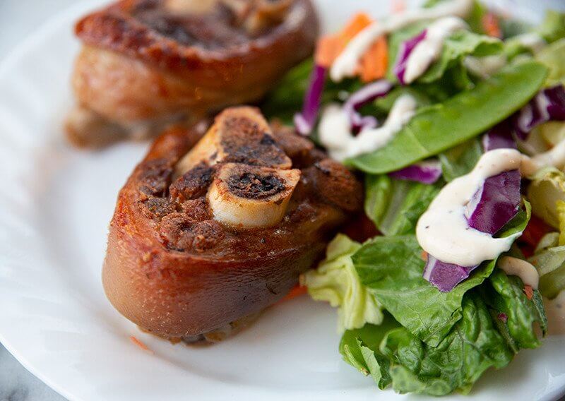 2 pieces Braised Ham Hocks in a white plate with some cabbage leaf