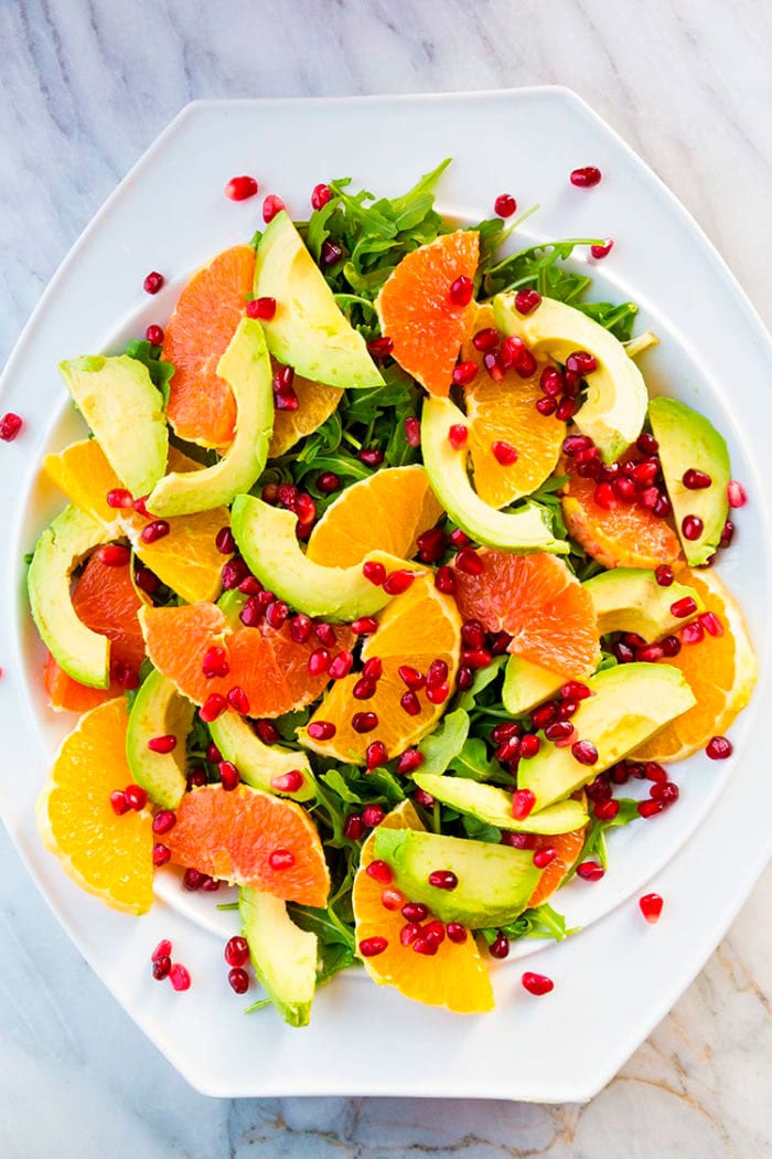 white bowl with arugula,  slices of orange,avocado,grapefruit and pieces of pomegranate