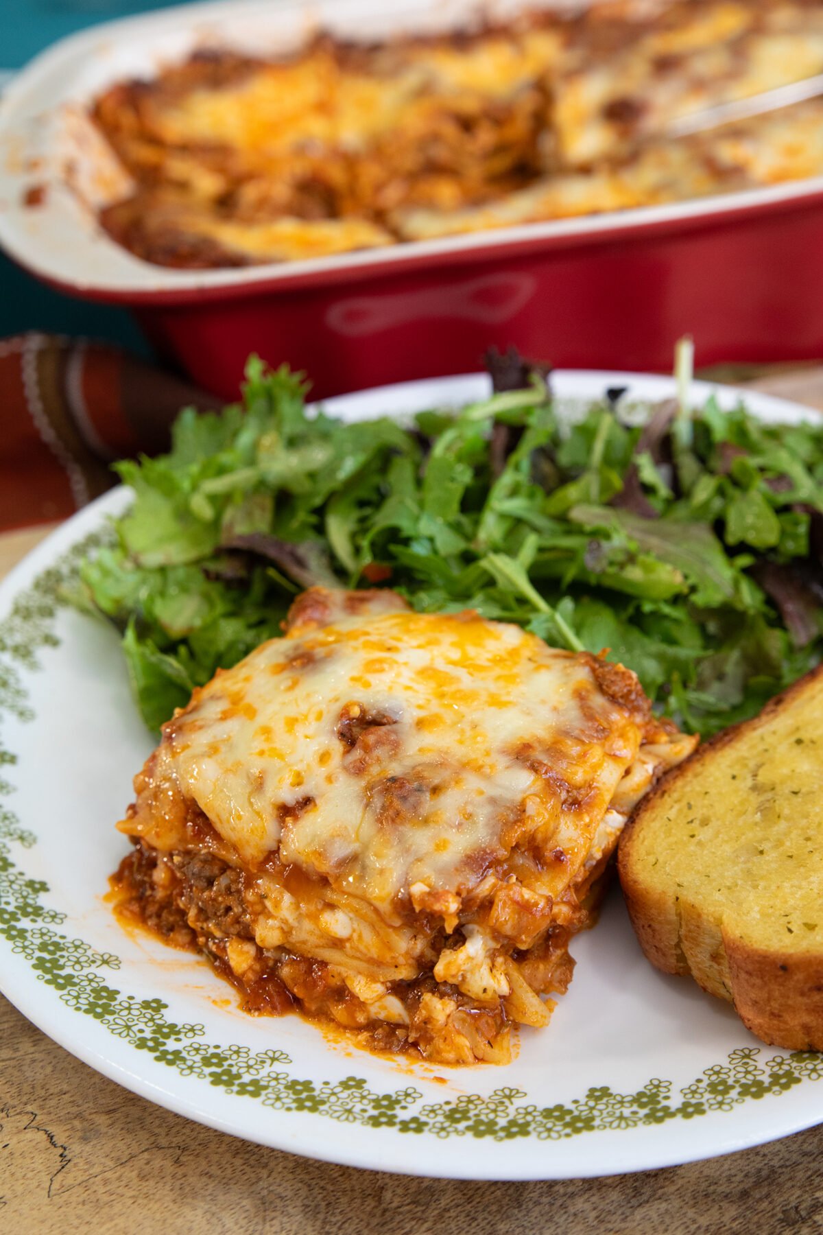 a slice of cottage cheese lasagna on a plate with salad and garlic toast