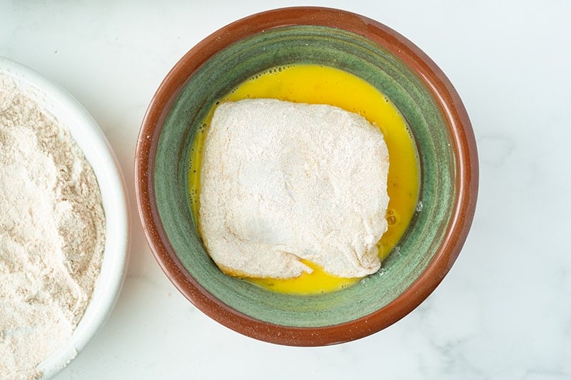 flour coated slice of raw chicken dipped in egg on a bowl