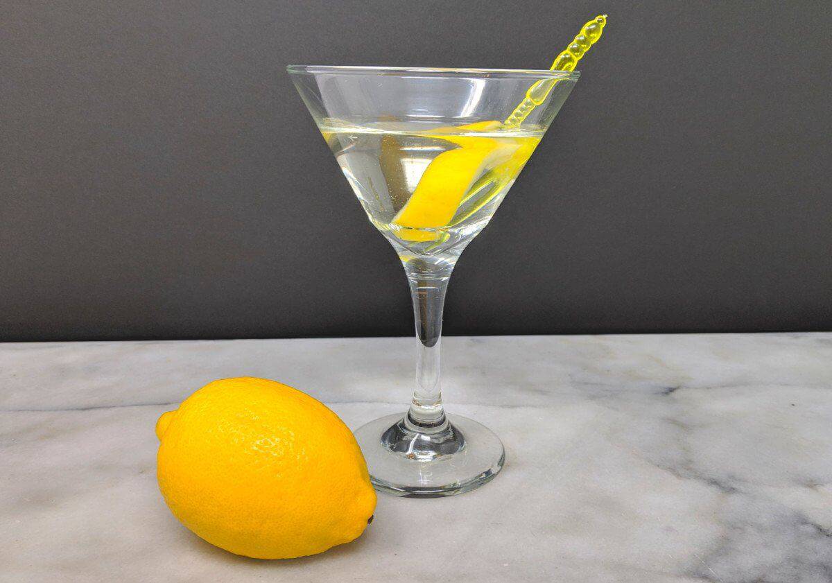 a glass of Vesper Martini garnish with a lemon twist and a fresh lemon on a marble table