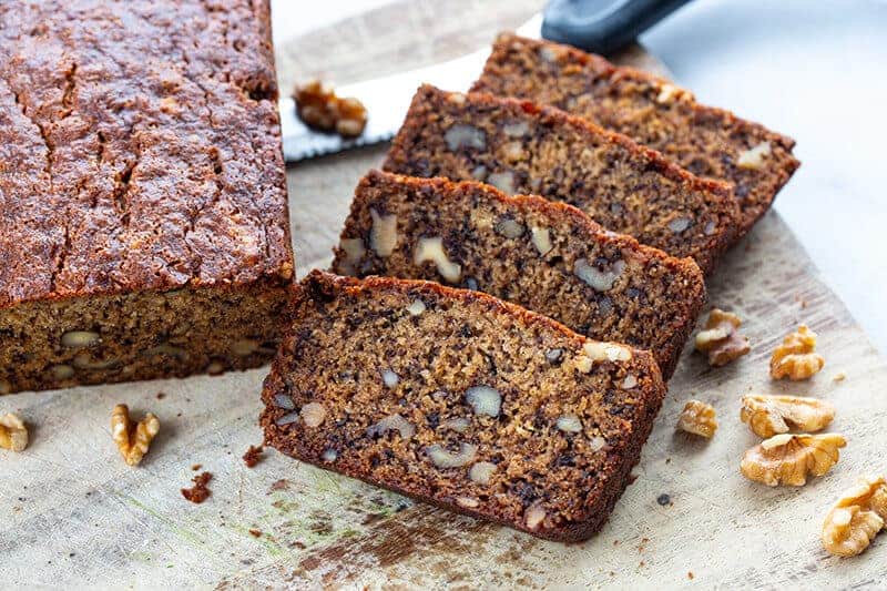 a loaf and slices of Banana Nut Bread in a wood cutting board