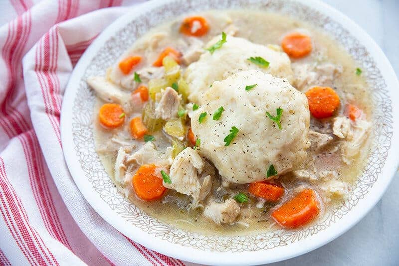 Chicken and Dumplings in a large white bowl with sauce and vegetables