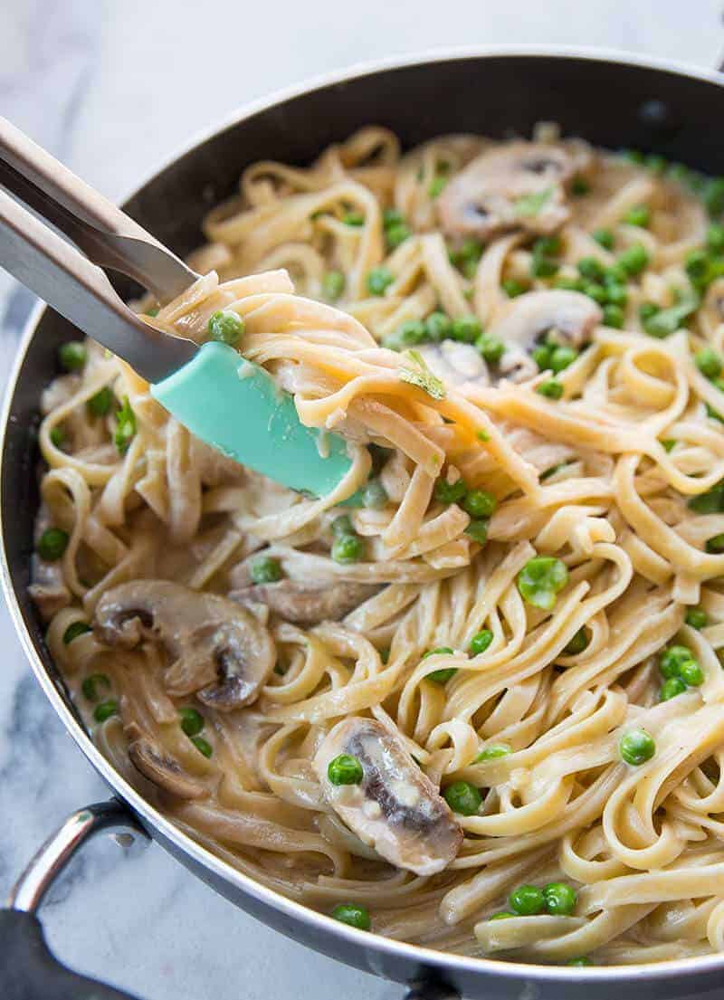 getting some Fettuccine noodles from Creamy Garlic Alfredo Sauce Fettuccine Skillet using kitchen tongs