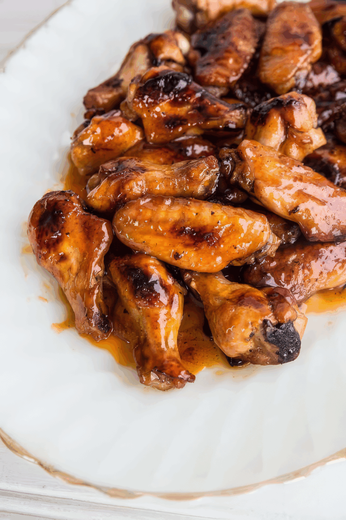 A close-up of hot wings piled on a white plate, showing a shiny, caramelized sauce coating and slightly charred edges.