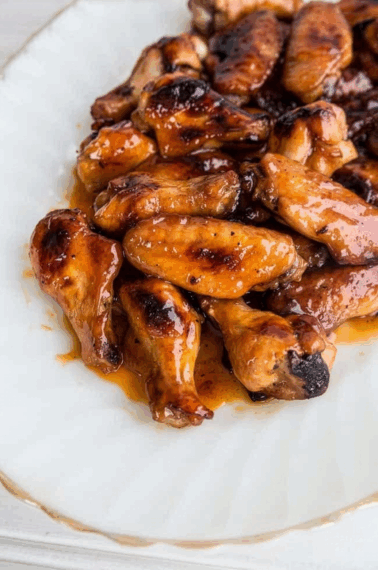 A plate of hot wings glazed with a shiny, caramelized sauce, arranged on a white dish. The golden-brown wings look juicy, flavorful, and irresistibly spicy.