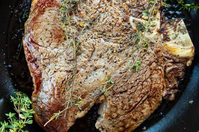 close up Porterhouse Steak in a red skillet with thyme springs on top