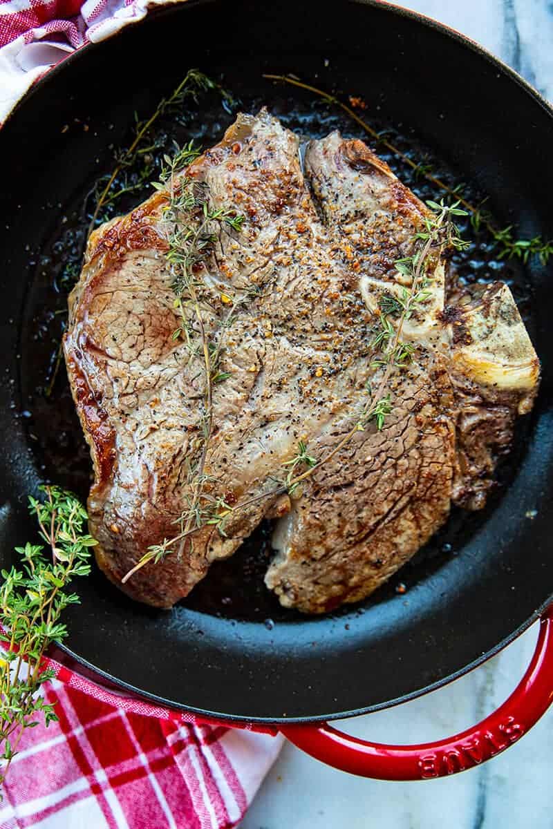 Porterhouse Steak in a red skillet with thyme springs on top