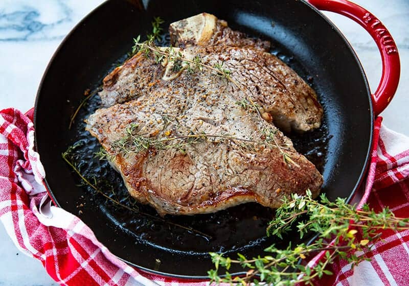 red checkered kitchen cloth underneath a red skillet with Porterhouse Steak 